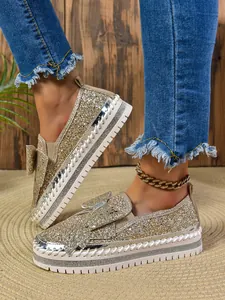 Glittery gold loafers with bow detail and rhinestone platform sole worn with denim
