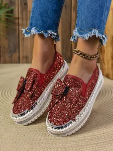 Close-up detail of women's red glitter loafers featuring a large bow and thick white sole