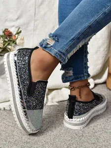 Detalle de mocasines con plataforma brillantes y pedrería con vaqueros azules rotos.