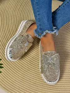 Close-up detail of gold sequin flat shoes featuring a large sparkling bow on a textured mat