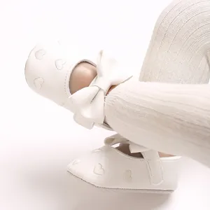 Gros plan de chaussures de marche bébé blanches avec cœurs brodés et grand nœud