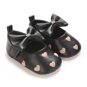 Détail de chaussures de marche pour bébé noires avec broderie cœur et grand nœud.