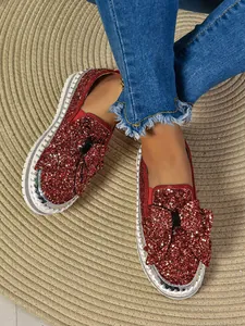 Detailed view of stylish red sequin loafers featuring a large bow and woven sole edge