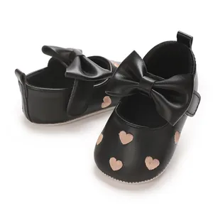 Vue de détail des chaussures de marche bébé noires avec cœurs et un grand nœud.