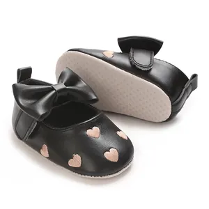 Détail de chaussures de bébé noires avec broderie cœur et grand nœud papillon