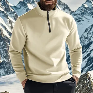 Gros plan d'un pull beige pour homme à col montant devant des montagnes enneigées