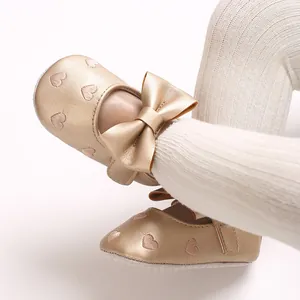 Vue détaillée de chaussures de bébé dorées avec cœurs brodés et un grand nœud.