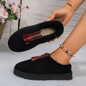 Detalle de pantuflas de invierno negras con cálido forro de piel sintética y borla étnica.