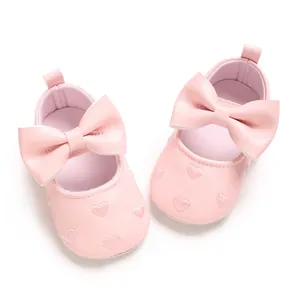 Détail de chaussures bébé roses avec cœurs brodés et un grand nœud élégant.
