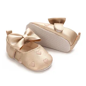 Détail de chaussures bébé dorées avec des cœurs brodés et un grand nœud élégant