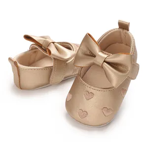 Détail de chaussures dorées pour bébé avec cœurs brodés et grand nœud élégant.