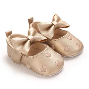 Gros plan de chaussures de bébé dorées avec cœurs brodés et grand nœud élégant