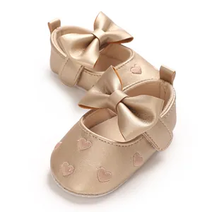 Vue détaillée des chaussures de marche pour bébé dorées avec broderie cœur et grand nœud.