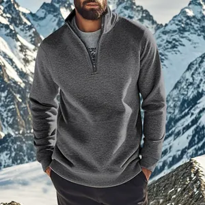 Sweat-shirt homme gris foncé à quart de zip posant dans un paysage de montagne