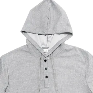 Détail d'un t-shirt Henley gris à capuche en maille gaufrée pour homme avec boutons noirs.