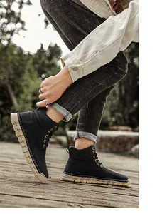 Lifestyle shot of black high-top outdoor boots with distinctive tan wavy soles.