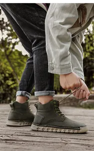 Detail of a man tying laces on green handmade stitched high-top outdoor boots outdoors.