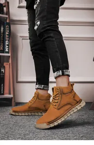 Side view of hand-stitched brown leather outdoor boots for men styled with black denim