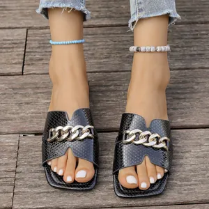 Detailansicht schwarzer flacher Sandalen mit Schlangenmuster und Goldkette an eckiger Zehe.
