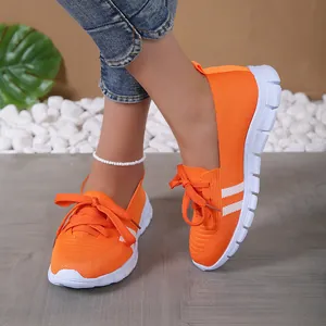 Lightweight women's orange fly-knit casual sneakers with white sole worn by a model