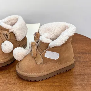 Cozy brown girls' snow boots with white faux fur lining and cute pom-poms on wood.