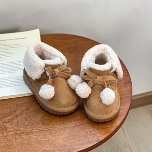 Warm brown girls' snow boots with faux fur lining and pom-poms on a wooden table.