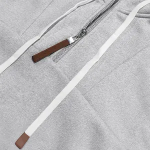 Detail van een grijze hoodie met zilveren halve rits en witte trekkoorden met bruine tips.