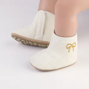 Nahaufnahme von weißen gesteppten Baby-Winterstiefeln mit goldener Schleife für Wärme