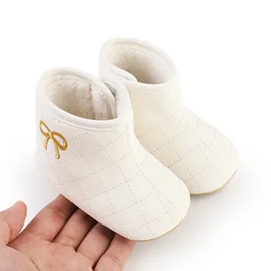 Nahaufnahme der weißen gesteppten Baby-Lauflernschuhe mit goldener Schleife und Fleecefutter