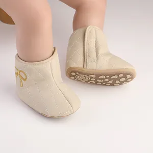 Nahaufnahme von beigen gesteppten Winterbabystiefeln mit gelber Schleife an Puppenbeinen