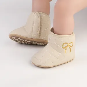 Detail der beigen gesteppten Baby-Winterstiefel mit goldener Schleife und weicher Sohle.