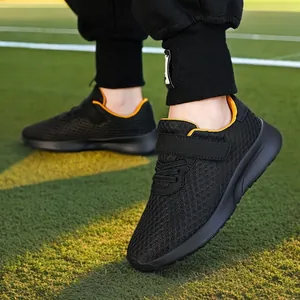 Zapatillas de running para niños de malla transpirable negra en campo de césped verde