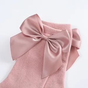 Detailed close-up view of pink baby socks with a large satin bow and soft knitted texture.