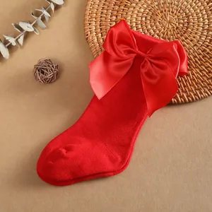 Detalle de calcetín rojo para bebé con un gran lazo de satén sobre un fondo rústico.