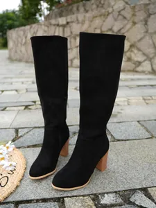 Classic black suede knee-high boots with stylish chunky heels on stone pavement.