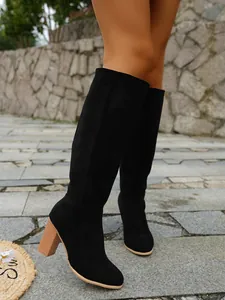 Close-up detail of stylish black suede knee-high boots with chunky heels worn outdoors