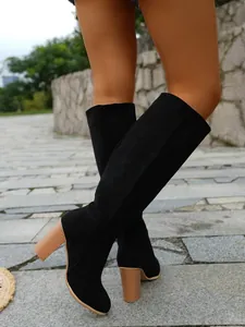 Elegant close-up view of black suede knee-high boots featuring chunky wooden heels