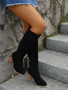 Detail view of black suede knee-high boots with chunky wooden-style heels on stone stairs