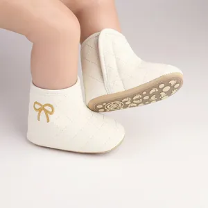 Close-up of white quilted infant walking boots with bow detail and non-slip soles.