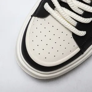 Close-up van zwart-witte leren platform sneakers met touwveters en geperforeerde neuskap.