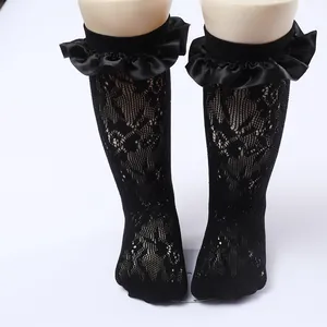 Close-up detail of children's black lace mesh socks with elegant ruffled satin trim