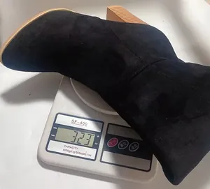 Detail showing weight of black suede over-the-knee chunky heel boot on a digital scale