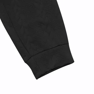 Macro view showing the detailed jacquard wheat-ear texture on a black tracksuit sleeve