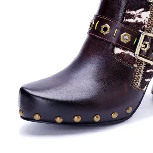 Close-up of hand-rubbed leather boot with metallic studs and belt buckle detail.