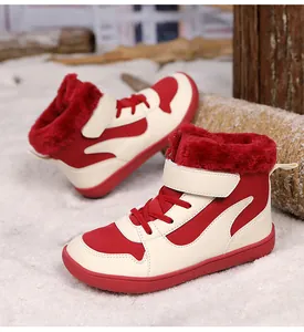 Primer plano de botas de invierno para niños con forro polar rojo sobre nieve artificial.