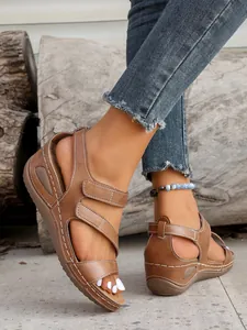 Close-up detail of women's brown wedge sandals featuring adjustable velcro straps and white stitching