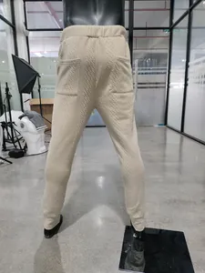 Detailed macro view of beige men's knitted trousers showing cable pattern and pockets