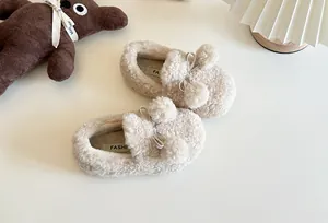 Detail showing fuzzy texture and pom-poms on kids' cream-colored winter loafers