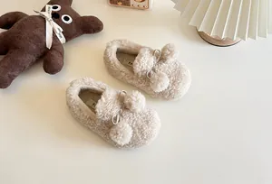 Close-up of beige children's fleece-lined slip-on shoes with fluffy pom-poms for winter.