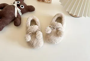Detailed view of plush children's loafers with fluffy pompoms and silver bows decoration.